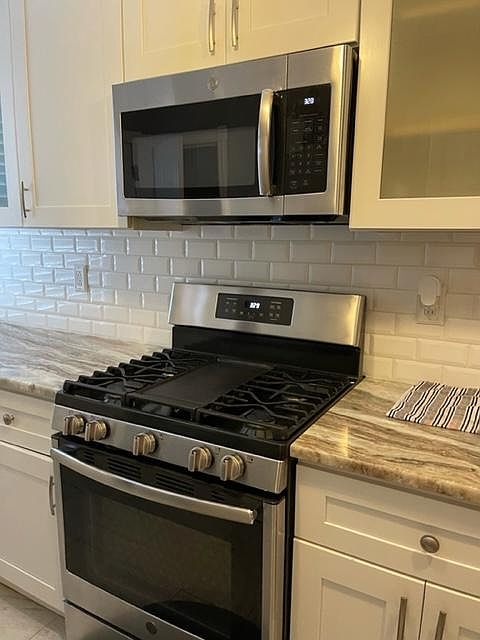View of stove, over the range microwave, glass front cabinetry and granite counter tops.