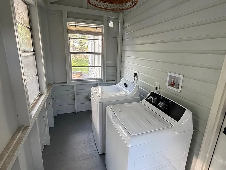 Dedicated laundry area with washer/dryer hookups, painted wood walls, and windows for ventilation and natural light.