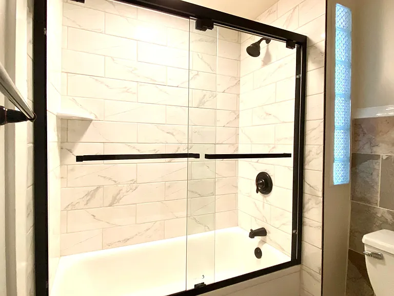 All new bathroom with tile shower, sliding glass door and black fixtures