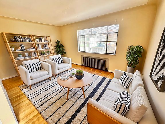 Bright and inviting living room with large window, chic white furniture, striped cushions, and stylish bookshelves.