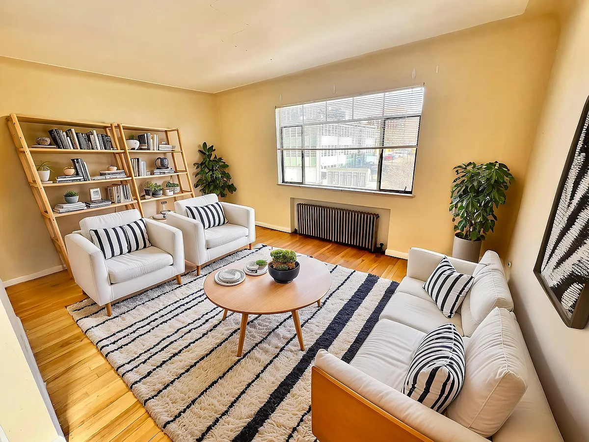 Bright and inviting living room with large window, chic white furniture, striped cushions, and stylish bookshelves. - Hillside Apartments