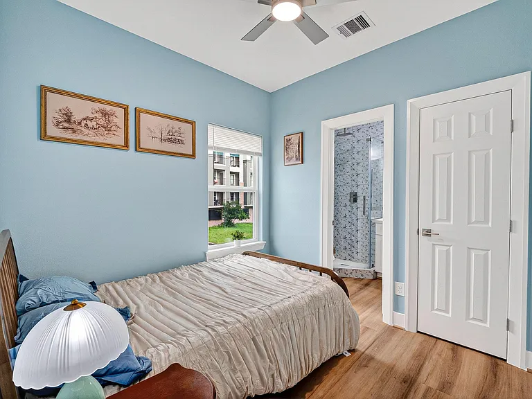 Well-sized bedroom with wood-look floors, ceiling fan, and a window for natural light; includes convenient access to an en-su