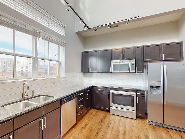 Apartment kitchen with stainless steel appliances, granite countertops and wood-style flooring.