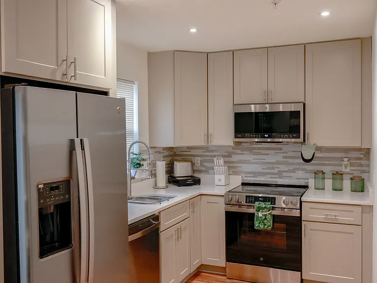Beautifully renovated kitchen featuring stainless steel appliances, custom cabinetry, modern tile backsplash, recessed lighting, and warm hardwood flooring throughout.