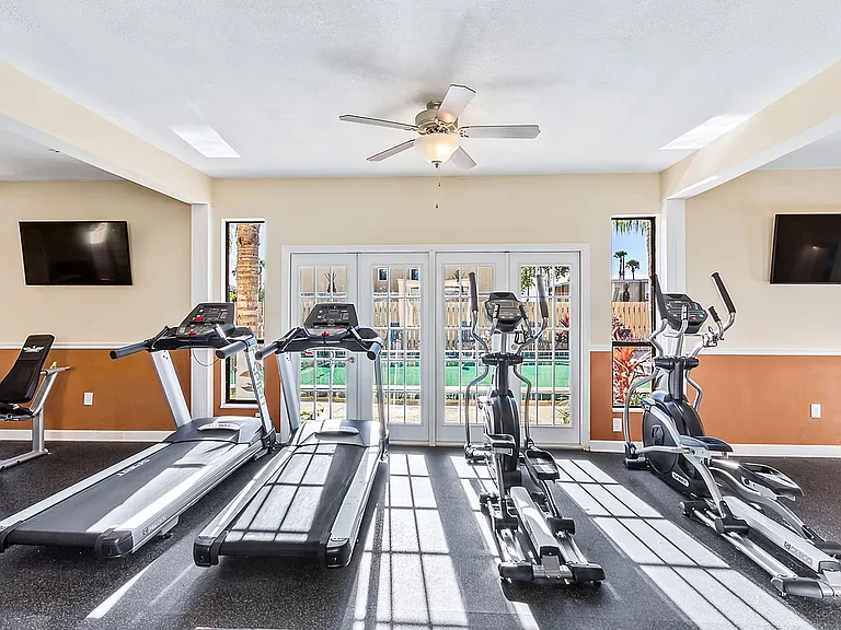 Bright and modern fitness center featuring treadmills and elliptical machines with a view of the outdoor pool through large windows.