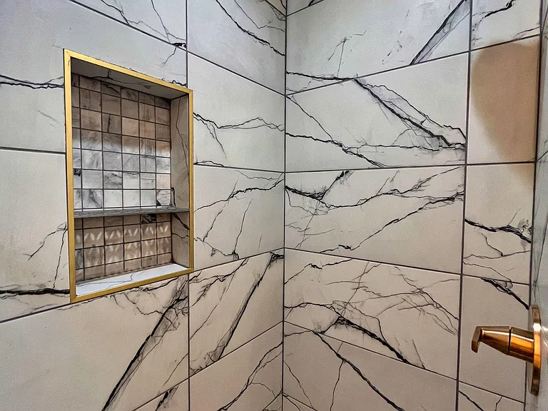 Walk-in shower with large-format marble-look tile, rain-style showerhead, and built-in niche for convenient storage.