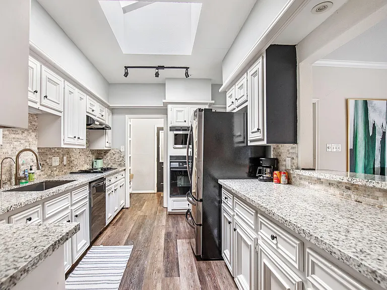 Galley kitchen with abundant white cabinetry, granite-style counters, mosaic backsplash, and full appliance set.