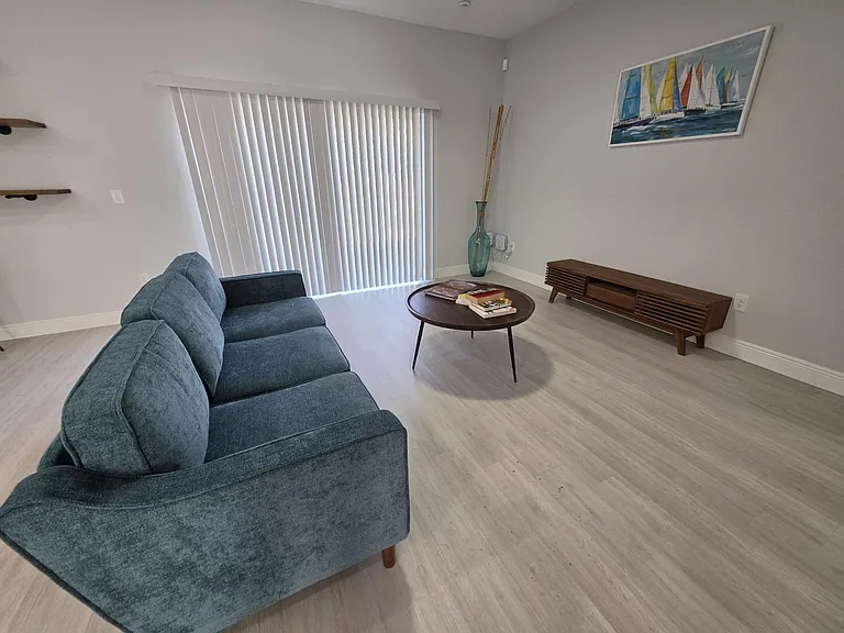 Open living area with a comfortable seating setup, media console, and large sliding doors with vertical blinds.
