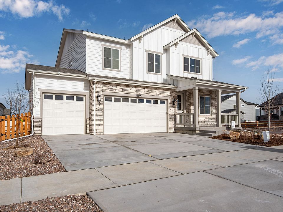 A two-story white house with a garage, surrounded by a paved driveway and a grassy yard against a bl