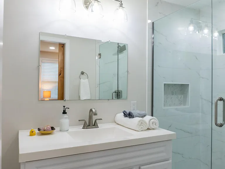 Bathroom with wide vanity and mirror lighting, plus a glass-enclosed walk-in shower and built-in niche storage.