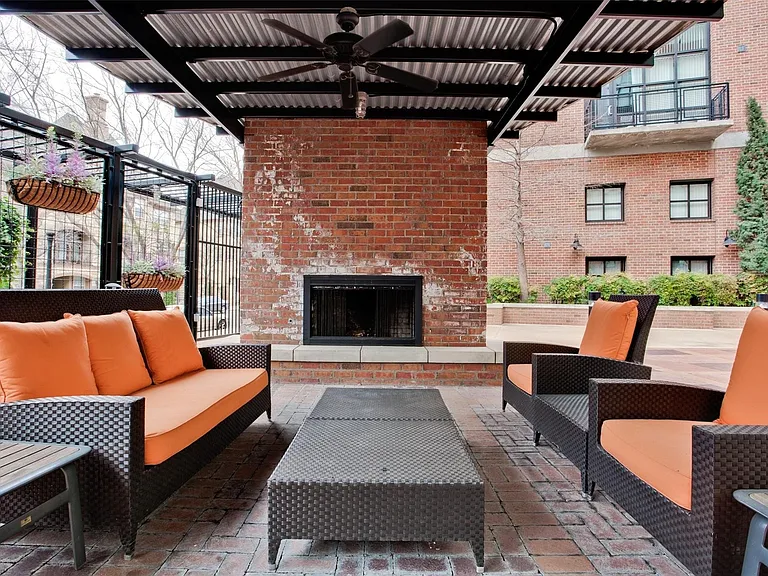 Outdoor patio featuring a brick fireplace with a black metal firebox, a corrugated metal awning, and an attached ceiling fan