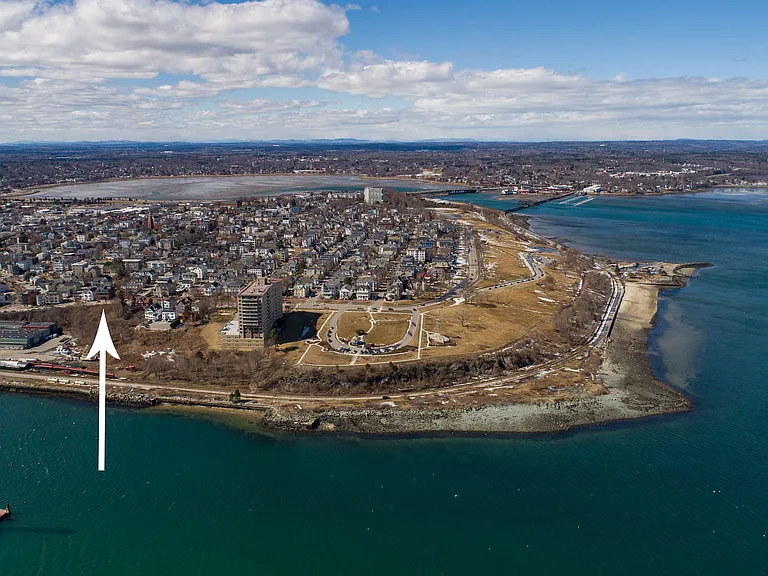 Drone shot with arrow pointing to building, parks and walking trails around the perimeter. (Early spring, grass not yet green.)