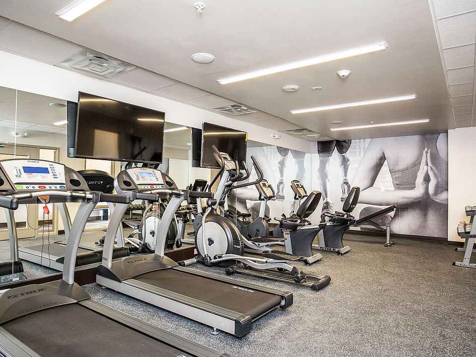 Modern fitness center with cardio machines, weights, and wall-mounted TVs.