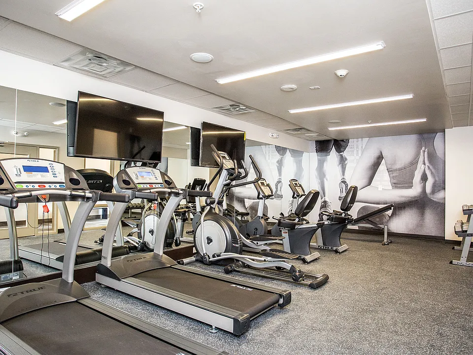 Modern fitness center with cardio machines, weights, and wall-mounted TVs.