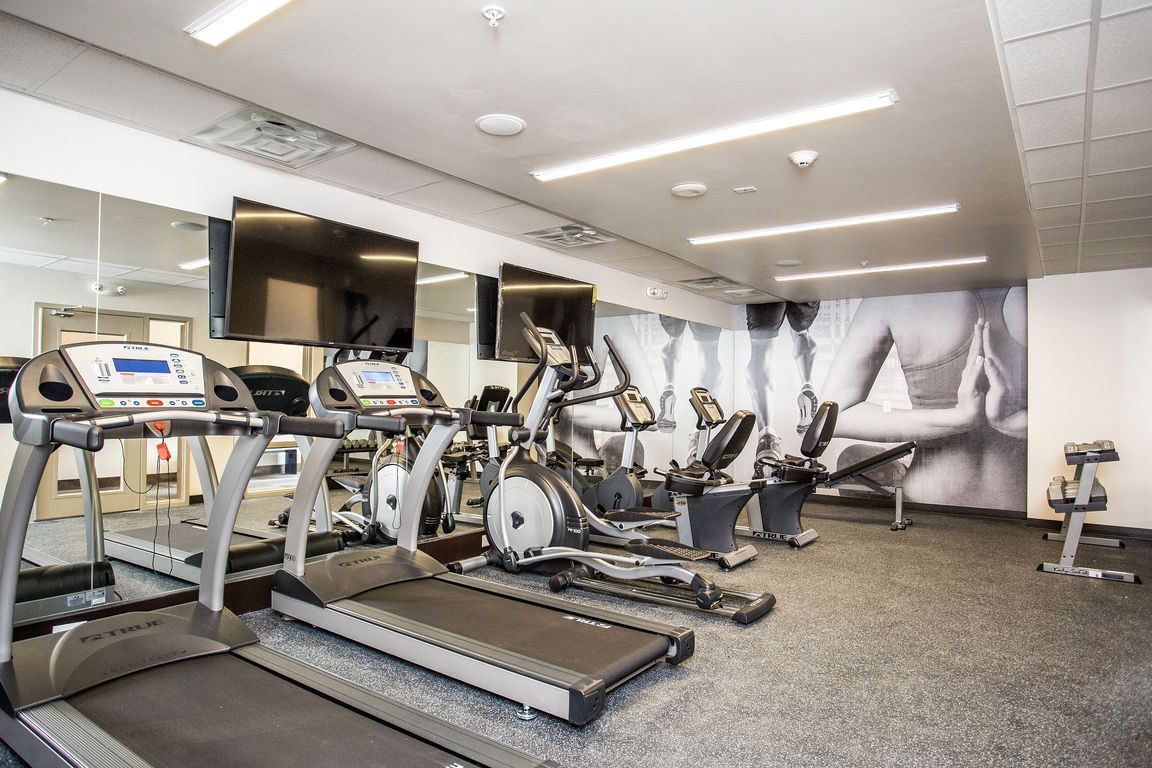 Modern fitness center with cardio machines, weights, and wall-mounted TVs.