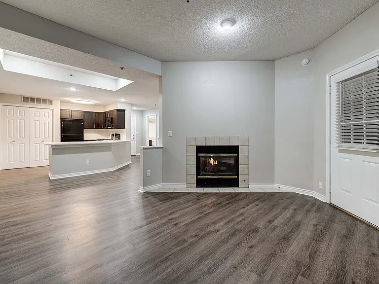 Inviting open-plan living area showcasing elegant wood flooring, a cozy fireplace, and a modern kitchen with dark cabinetry.