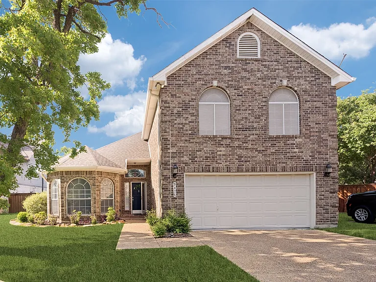 Brick facade residence featuring an attached garage, arched windows, and a manicured lawn