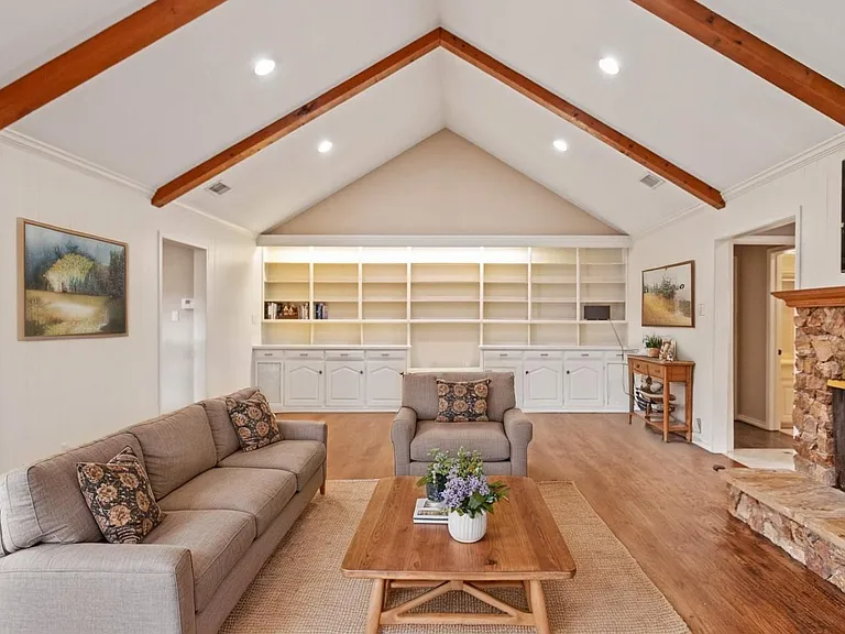 Open concept living with tall beam ceiling and built in cabinets and shelves with fireplace.