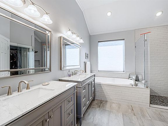 Sophistication and elegance are showcased in this late 2019 remodeled primary bathroom. These handsomely crafted dual vanities possess soft-closing cabinetry, brushed nickel fixtures and Carrara marble countertops. The cool gray tones of the tile, wo