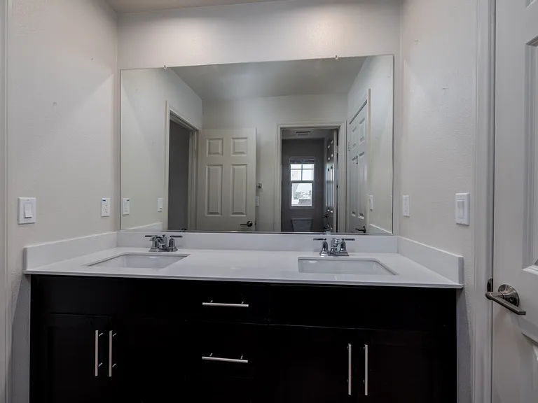 Elegant shared upstairs bathroom featuring dual sinks with dark wood cabinetry, offering direct access from both bedrooms. The modern design and ample storage create a luxurious and functional space perfect for daily convenience.