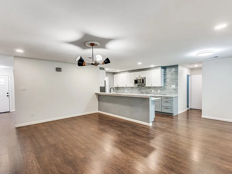 Expansive open-concept space featuring rich wood-finish flooring, recessed lighting, and a modern chandelier