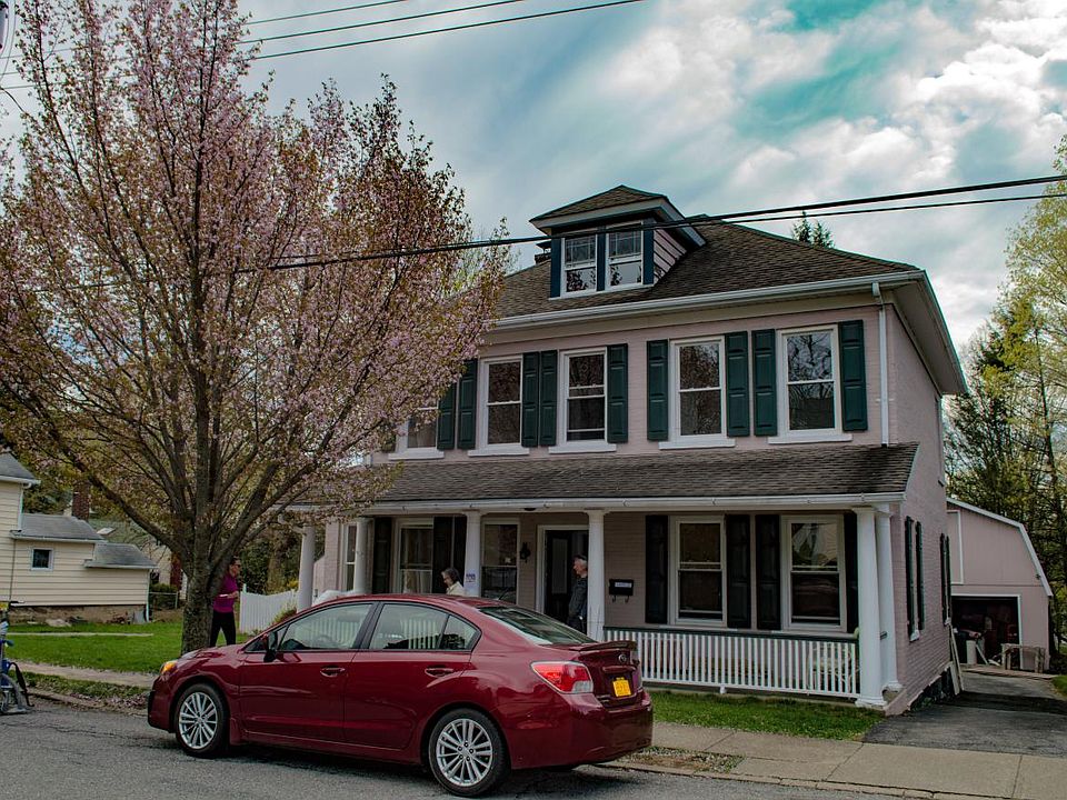 House in late April w/cherry tree. Attic dormer above. Porch below.