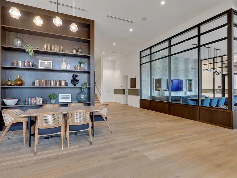 Modern communal area with elegant bookshelves and sophisticated dining setup, featuring stylish lighting and an open-plan meeting room.