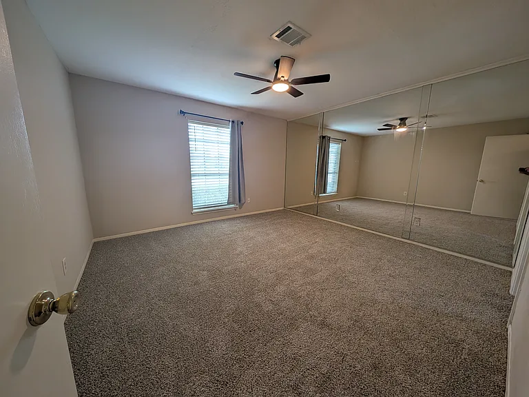 The master bedroom highlighted with wall to wall mirrors, new carpet, and fan.