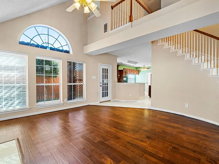 Vaulted living space featuring rich wood-finish flooring, a ceiling fan with integrated lighting, and a prominent arched window above a trio of windows