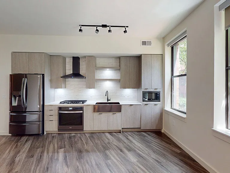 Apartment kitchen with black stainless steel appliances, quartz countertops, wood-style flooring, and custom Italian cabinetry.