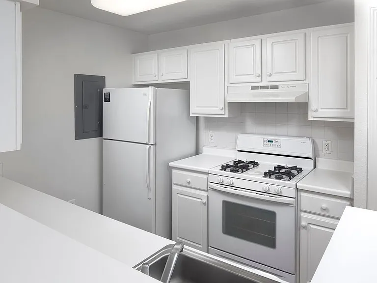 Wilmington West Classic Package kitchen with white cabinetry and appliances, white or beige laminate countertops, and white tile backsplash. Select homes include stainless steel appliances and hard surface flooring in common areas