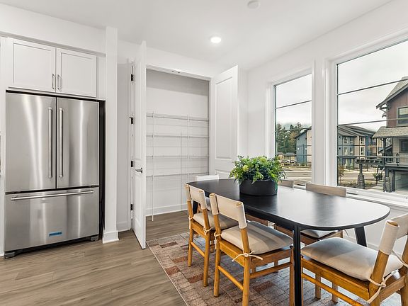 A modern, bright kitchen with stainless steel appliances, a wooden dining table, and chairs, set aga