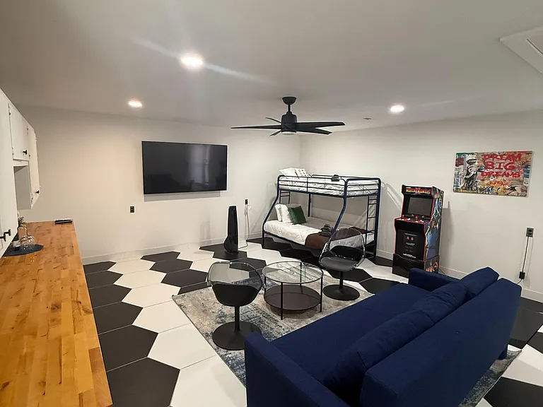 Open-concept studio-style bedroom with 2 beds (full & Twin) , seating area, ceiling fan, and bold tile flooring.