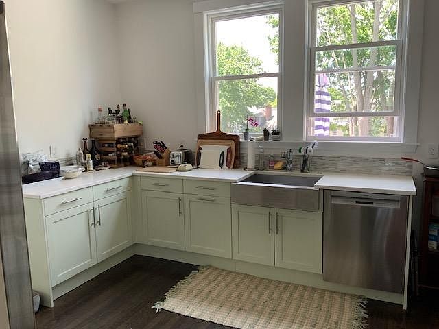 Chef's kitchen with oversize windows, high ceilings, deep stainless steel sink. Subtle mint green color on the soft-close, high-quality cabinets contrast with the dark stained wood floors.