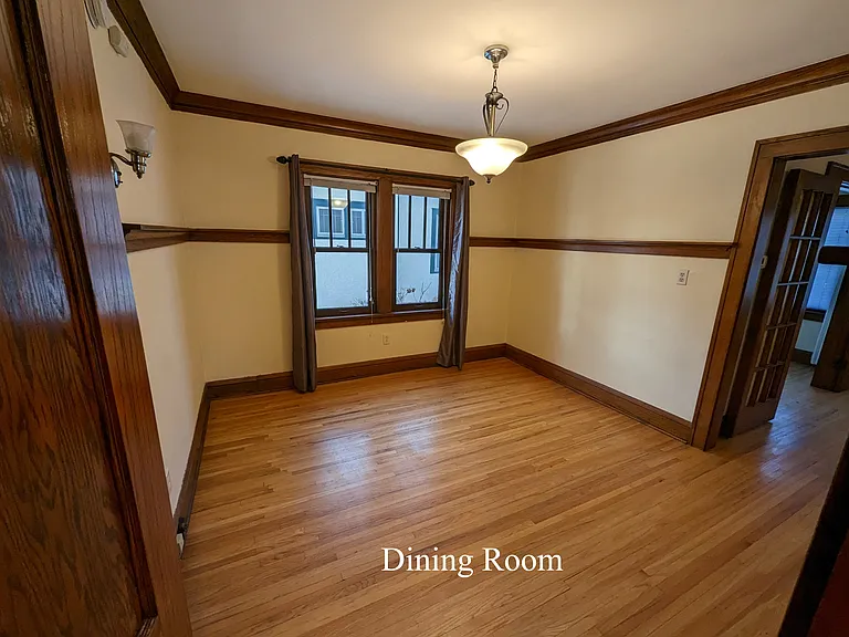 Dining room looking west from kitchen door with living room to the right north and 1st bedroom to the left south. Brown wood on walls is plate rail and coved ceiling.