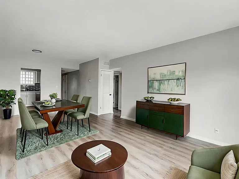 Contemporary dining area with stylish green chairs, a sleek wooden table, and modern art, seamlessly connected to a chic kitchen with black tile accents.