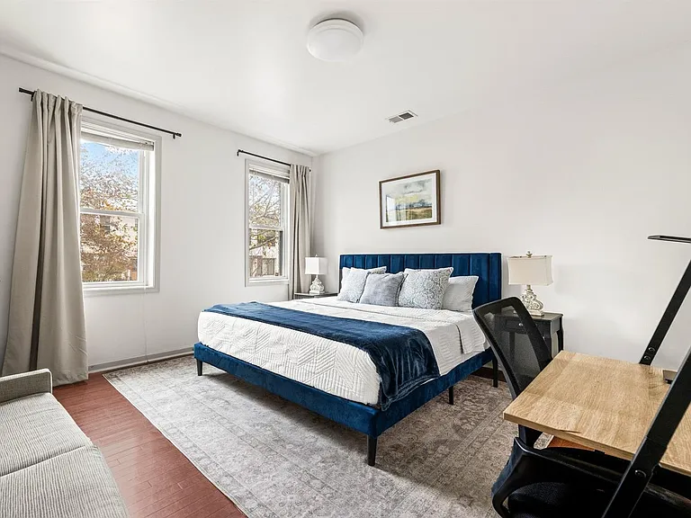 Spacious bedroom with two windows, a queen bed, nightstands, and a dedicated desk area for working from home.