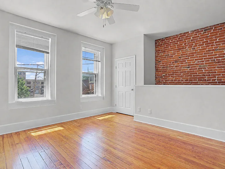 Bedroom with salvaged hardwood floors, oversized windows, a ceiling fan, and exposed brick