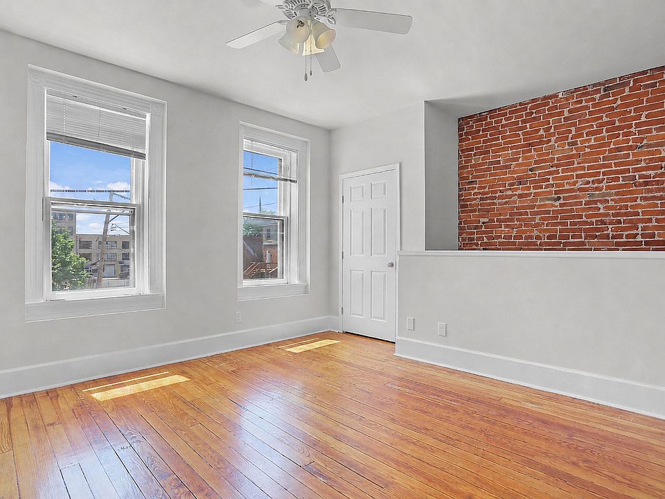 Bedroom with salvaged hardwood floors, oversized windows, closet, a ceiling fan, and exposed brick