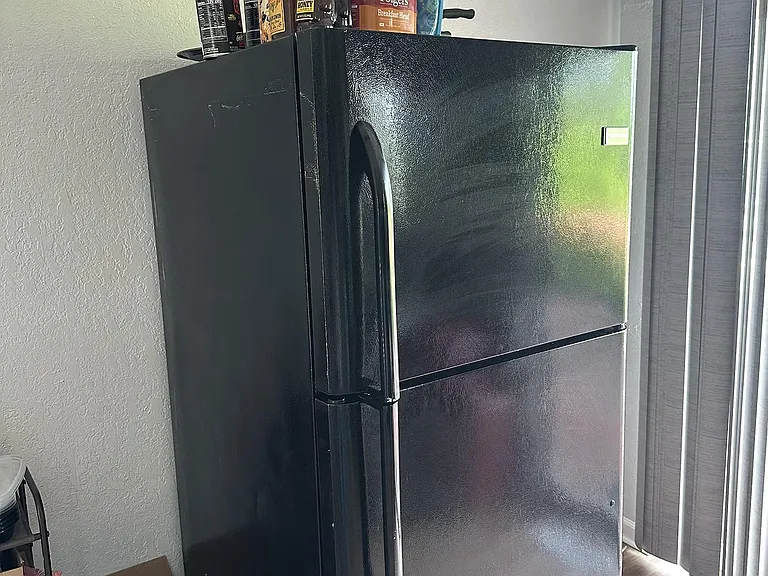 Full-size refrigerator provides convenient food storage near a sliding door with vertical blinds for easy access.