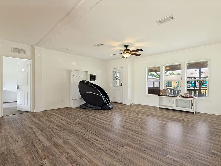 Spacious living area with durable wood-look flooring, ceiling fan, and large windows near the entry for easy flow.