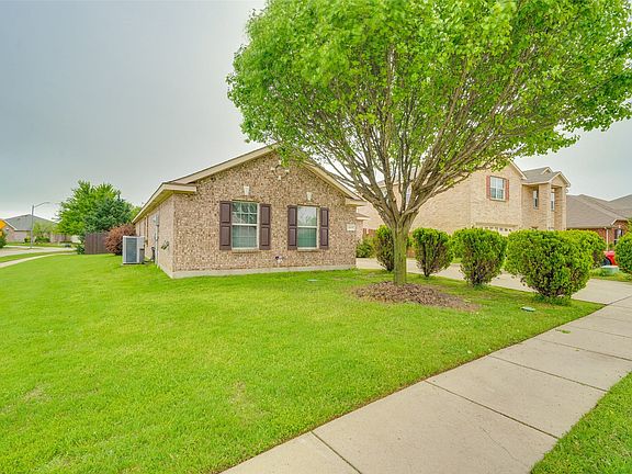 Brick exterior with brown shutters, mature shade tree, manicured shrubs, and a concrete sidewalk