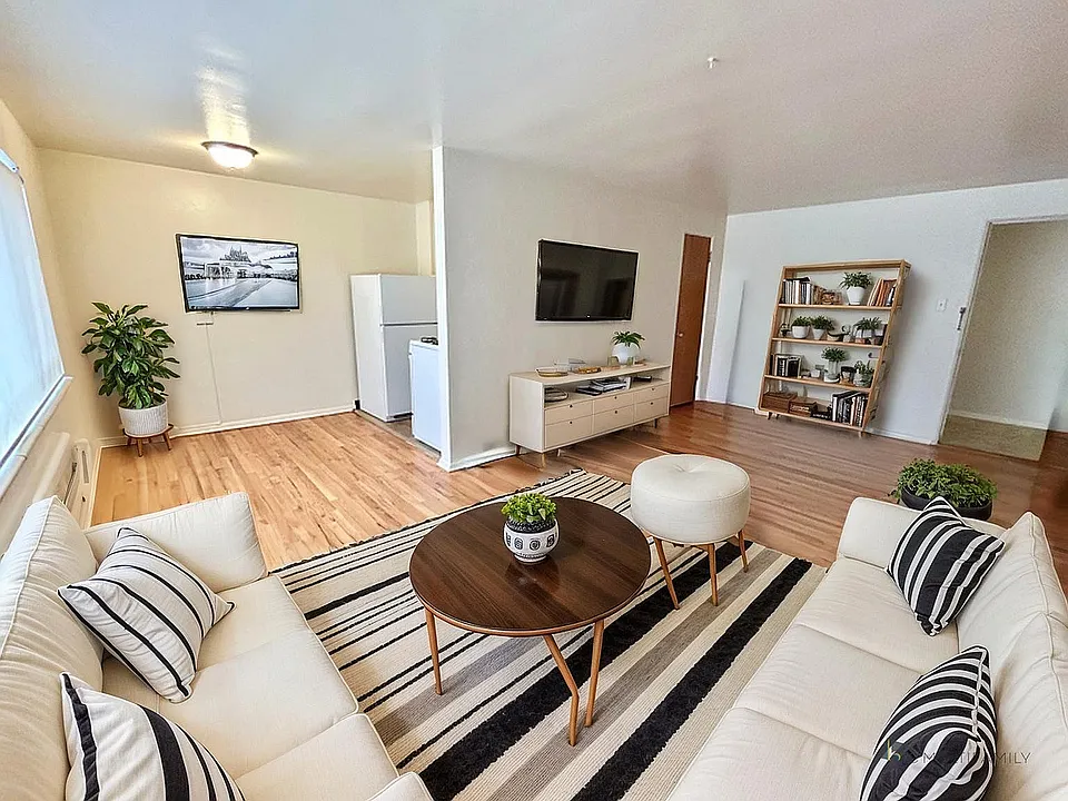 Charming living room with elegant decor featuring cozy sofas, a stylish striped rug, and lush greenery. Bright room with modern flat-screen TV and sleek wooden flooring.