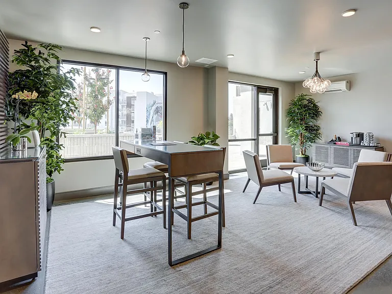 Light_filled coworking area with a high_top table, relaxed seating, and greenery throughout the room.