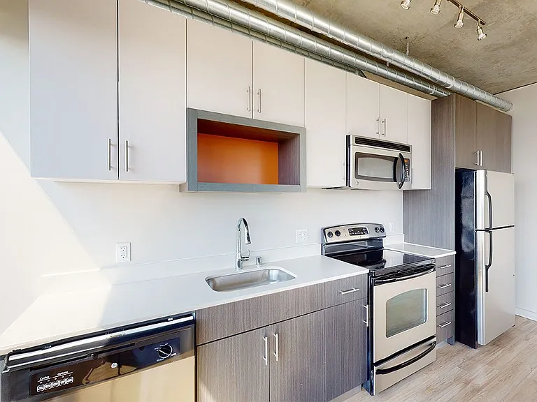Apartment kitchen with stainless steel appliances, quartz countertops and wood-style flooring.
