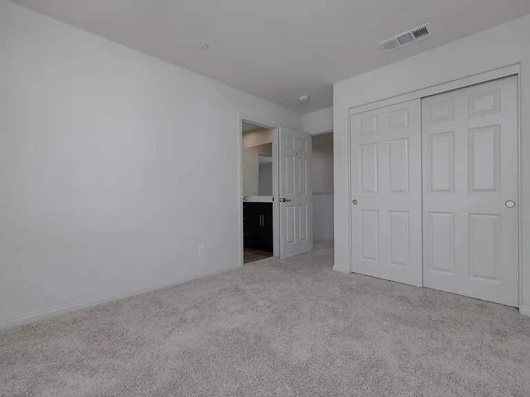 Another view of the second upstairs bedroom showing the main entry door and direct access to the shared bathroom. Features soft carpet flooring, ample closet space, and a bright, open layout ideal for comfort and privacy.