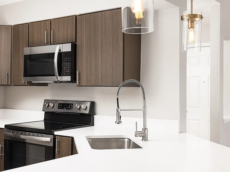 Modern apartment kitchen with elegant white countertops, stainless steel appliances, and warm wood flooring.