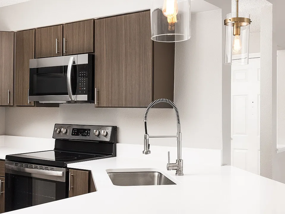 Modern apartment kitchen with elegant white countertops, stainless steel appliances, and warm wood flooring.
