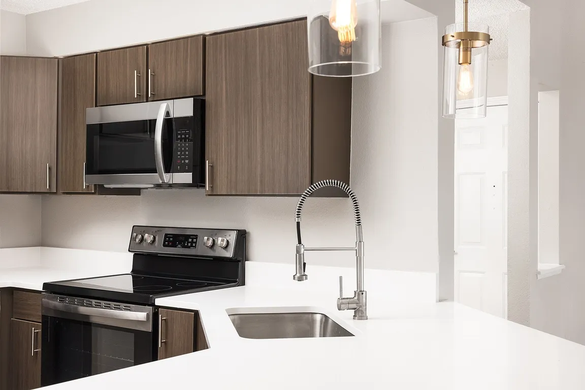 Modern apartment kitchen with elegant white countertops, stainless steel appliances, and warm wood flooring.