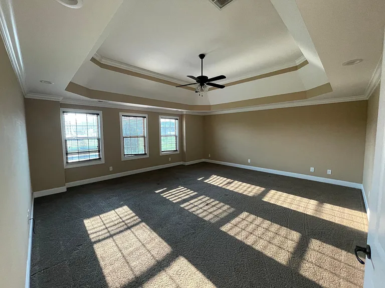 Spacious bonus room with elevated tray ceilings, abundant natural light, and backyard outlook and a closed door for privacy making it a versatile space.
